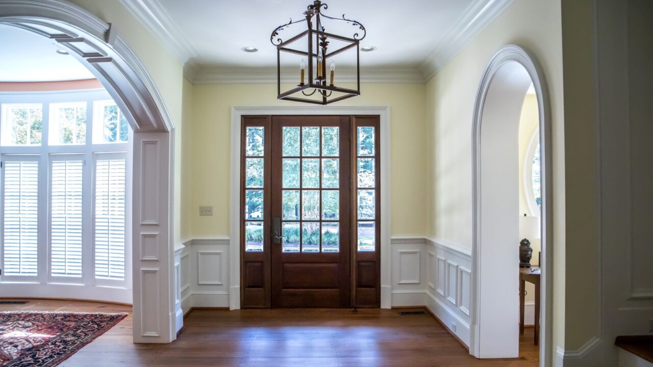 Front entrance foyer hallway of a large home house with yellow walls and a wood door with windows and a large custom lighting fixture