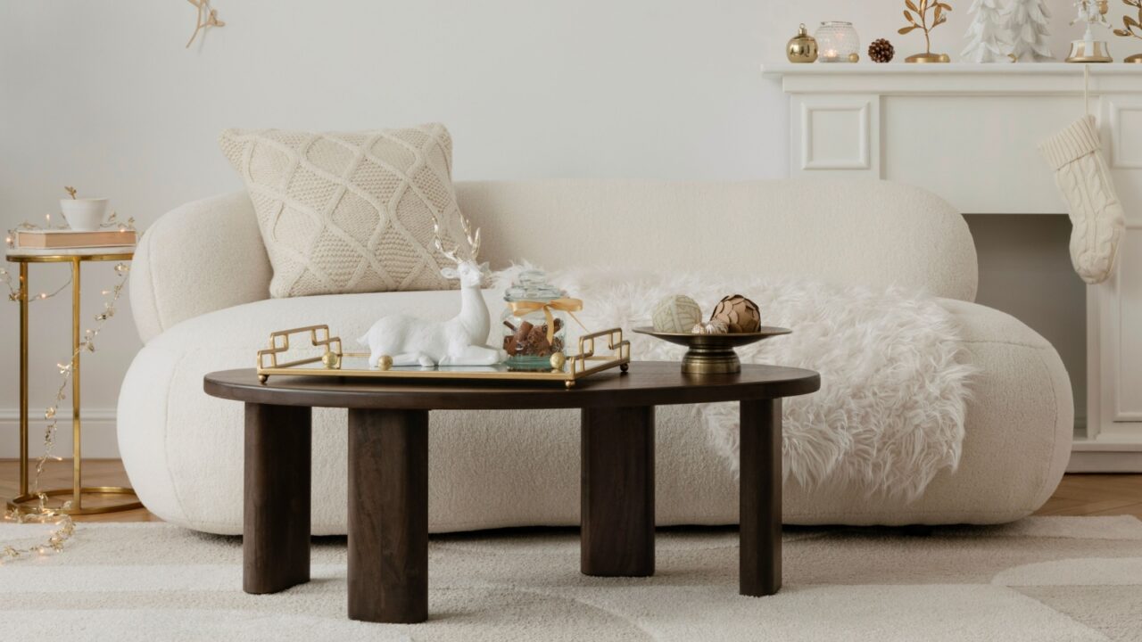 A cozy living room with a plush white couch, a round dark wooden coffee table with decorative objects, and a small golden side table.