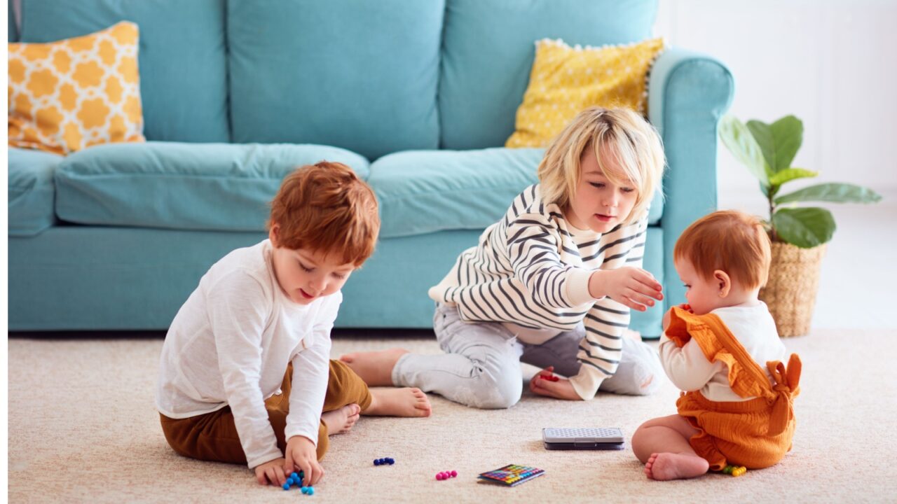 Three children playing at home on the floor with small toys.