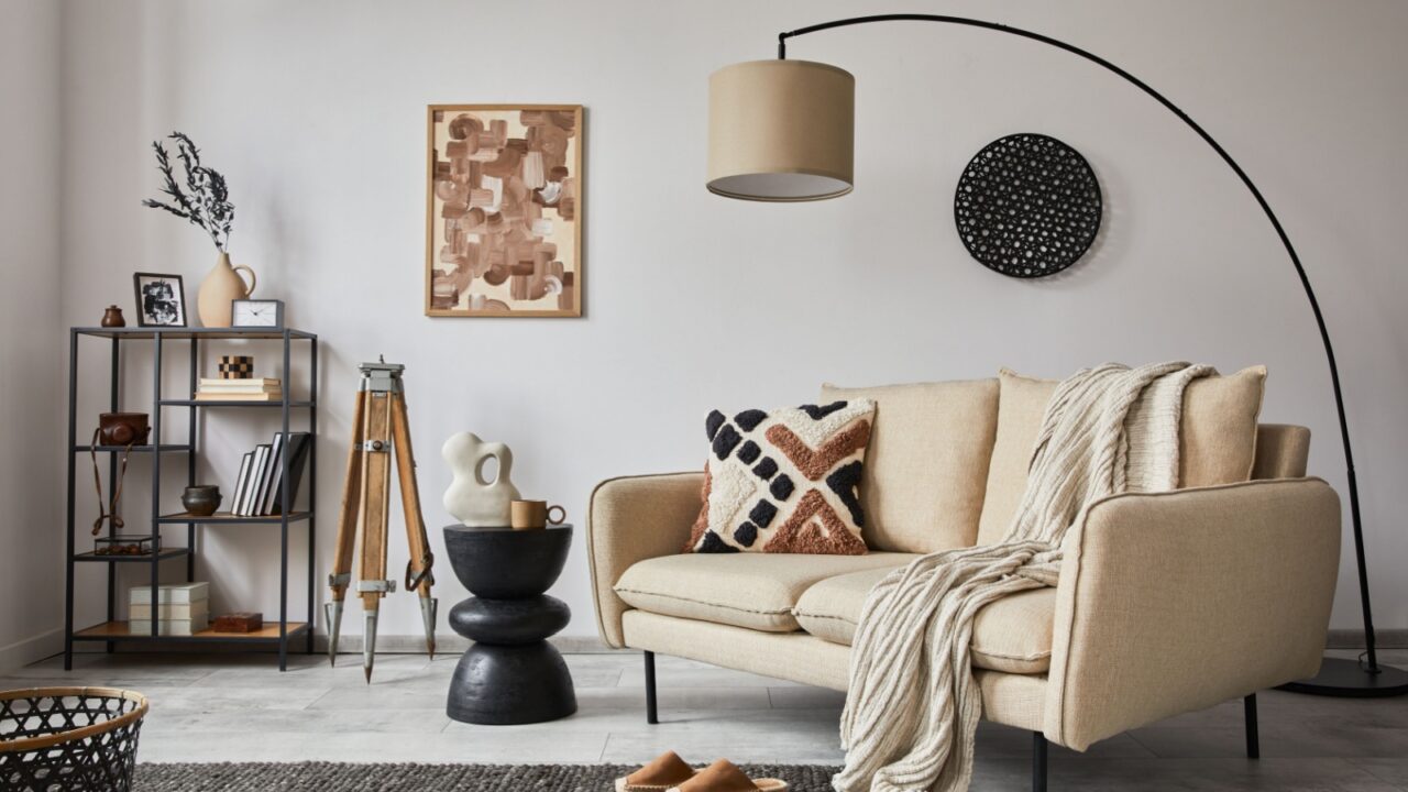 Elegant living room interior design with beige sofa, art wall frame, metal shelf with vintage vases and personal accessories.