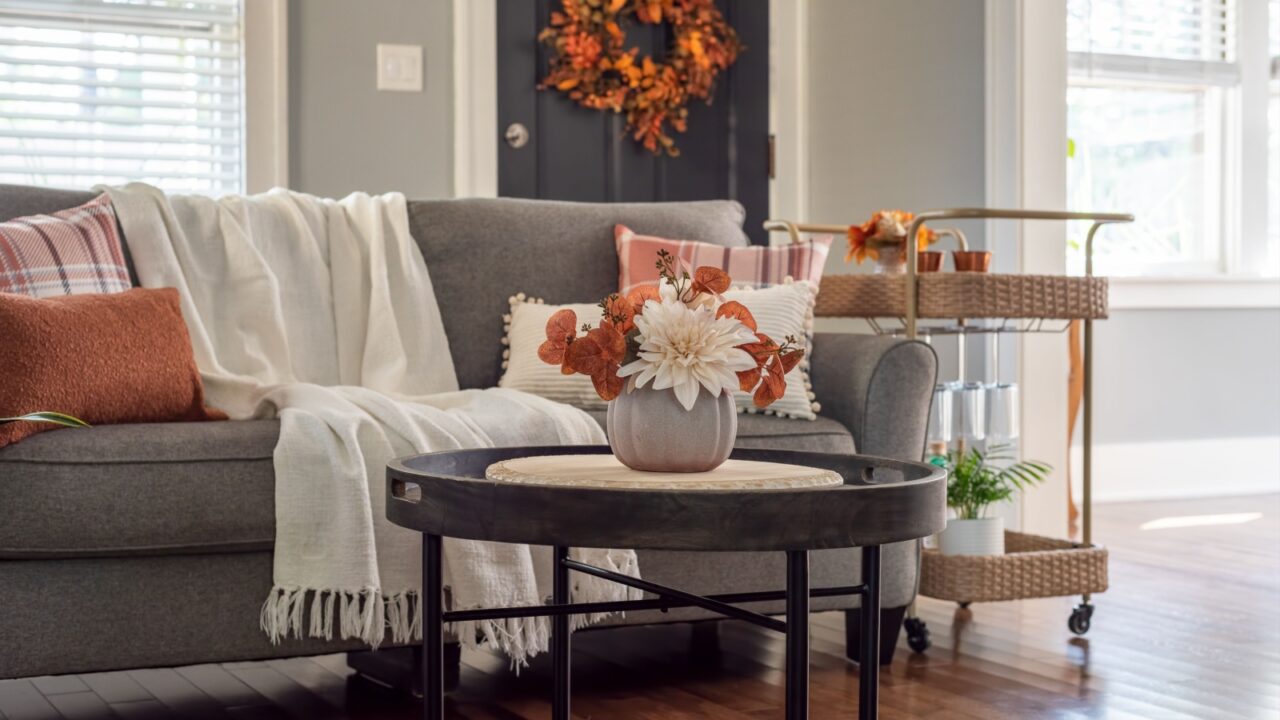 A cozy living room with a grey sofa, floral centerpiece on a coffee table, and a rattan basket trolley