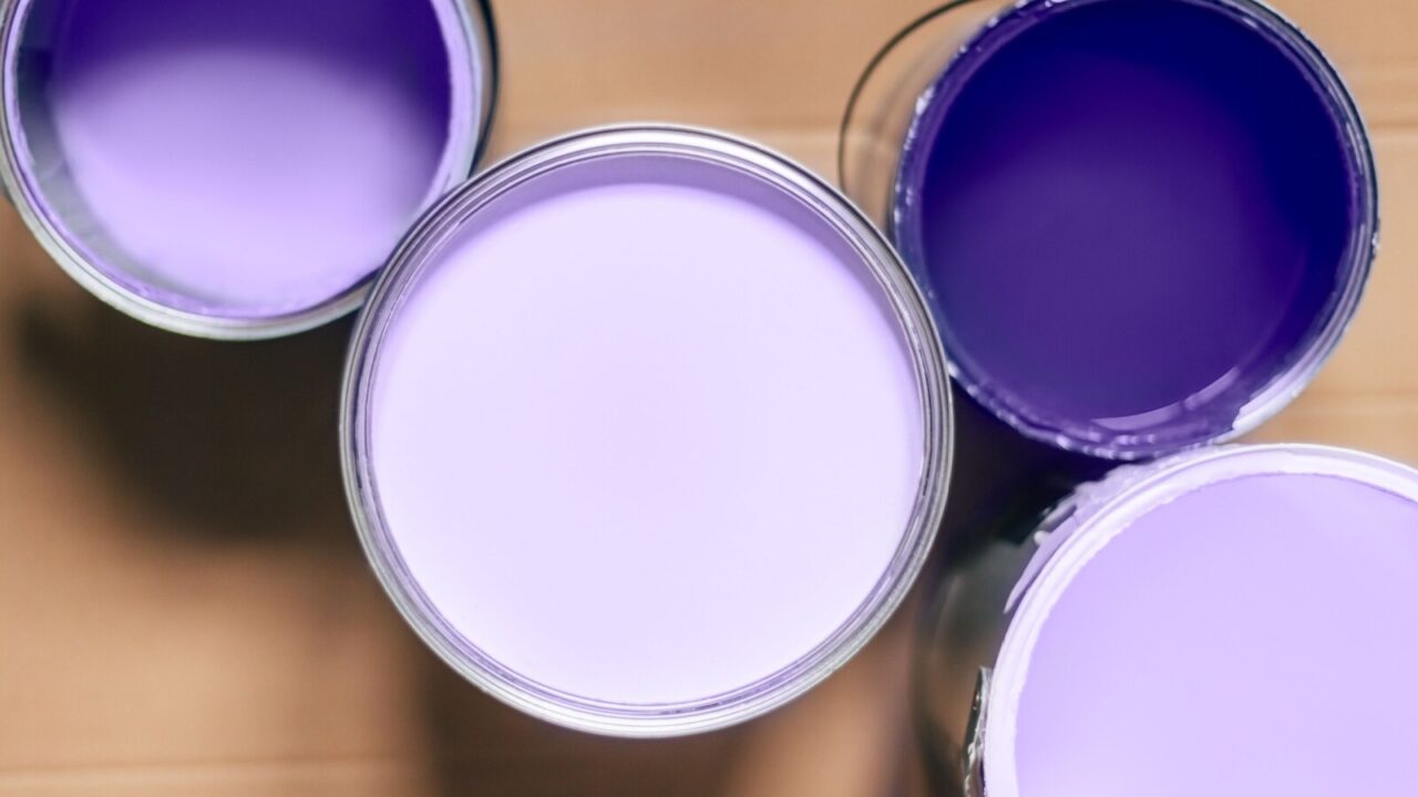 Four open paint cans of various shades of purple are placed on a wooden surface