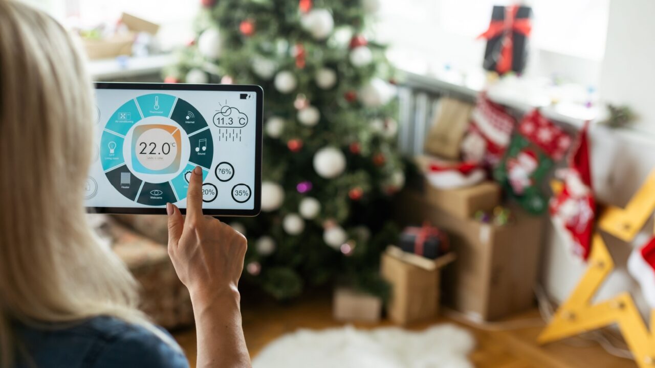 A woman using a tablet to control home settings with a Christmas tree and gifts in the background.