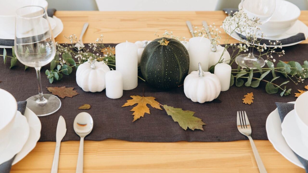 Thanksgiving dining table set up with brown table runner, green and white pumpkins, candles, and baby breaths