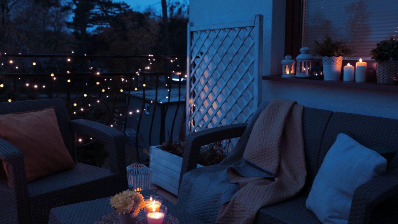 Cozy seating area in balcony during night time, decorated with string lights, candles, and lanterns