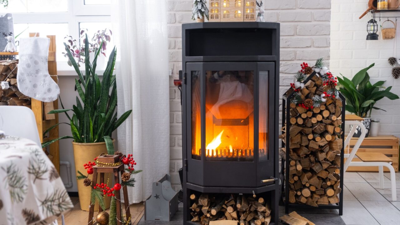 Metall black stove, burning hearth fireplace in white Festive interior of house is decorated for Christmas and New Year, Christmas tree.