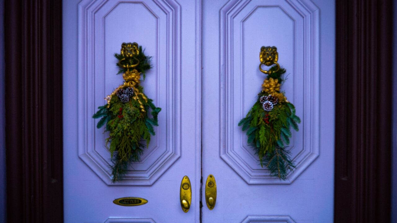 A purple front door decorated for Christmas with two swags hanging from lions head door knockers.