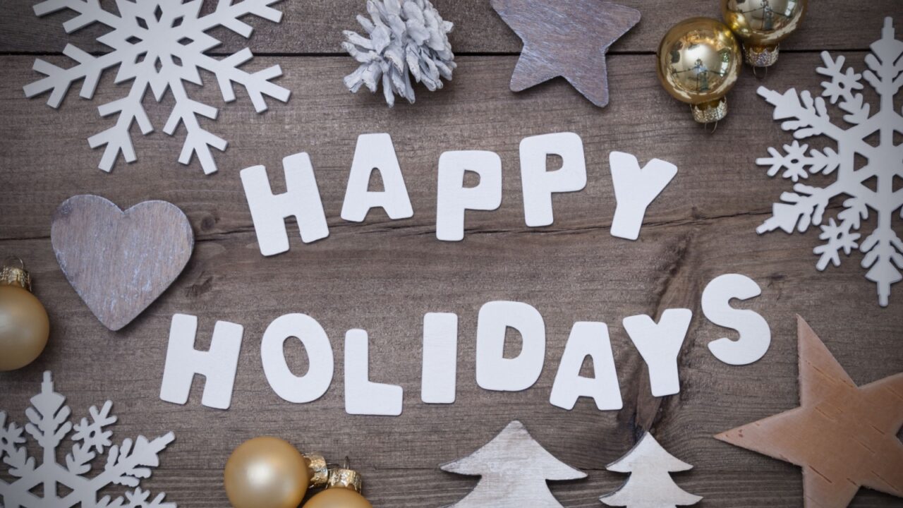 White letter paper cut outs of the word 'Happy Holidays' placed on a wooden table surrounded by decorative items and ornaments