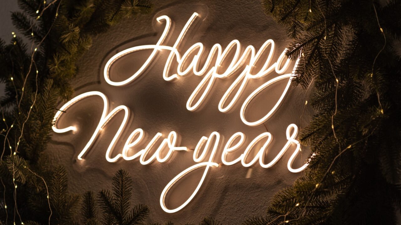 A glowing neon sign of 'Happy New Year' hung up on a wall in the middle of a wreath.