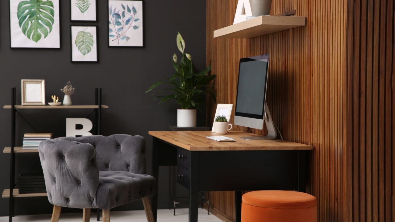 Comfortable workplace with computer near wooden wall in stylish room interior.