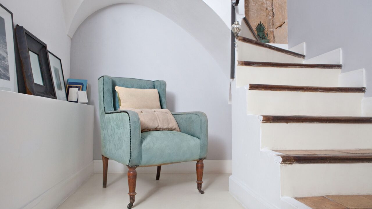 an elegant armchair in a stylish home with cushions under an arch and next to stone walls and stairs, indoors.