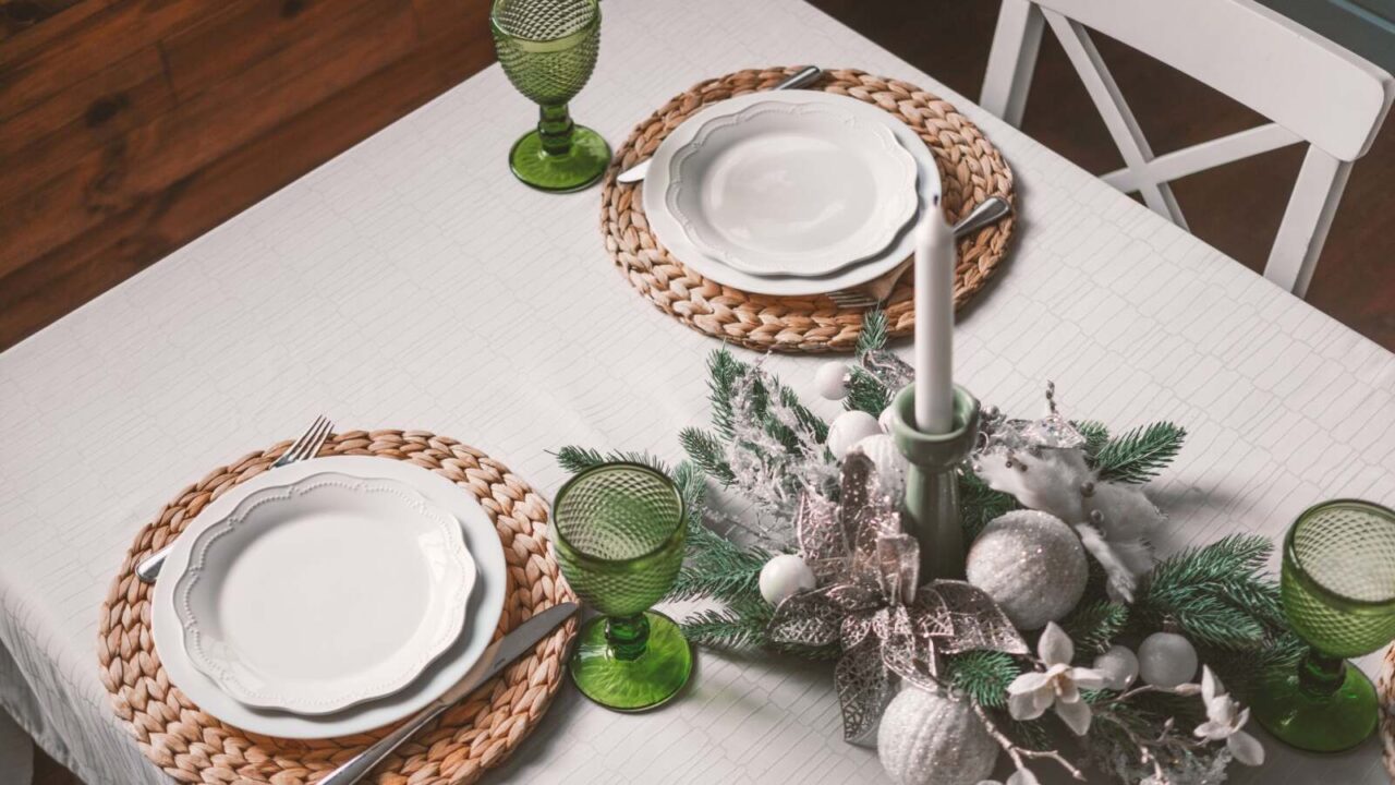 Dining table set up with plates, glasses, and a beautiful centerpiece made with ornaments, faux flowers, pine branch, and candle with candle holder