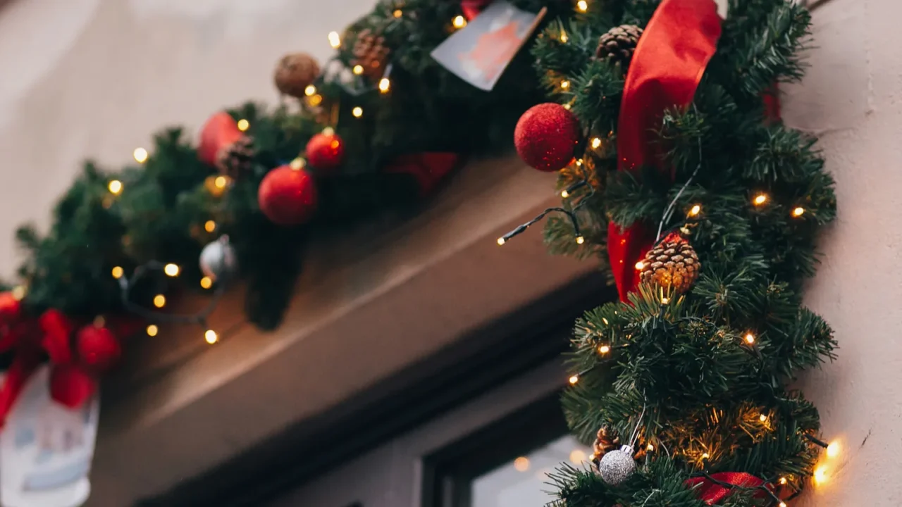 Stylish christmas decorations, garland lights and fir branches with ornaments on window in european city street