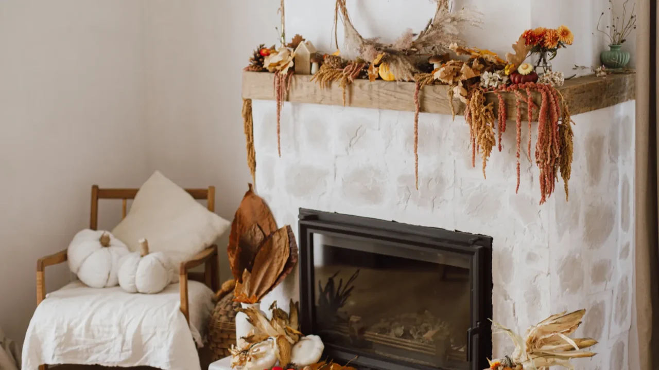 Stylish decoration of fireplace with pumpkins, wreath, autumn leaves, nuts, candle on rustic wood in modern farmhouse living room. Autumn fireplace mantel. Thanksgiving and Halloween