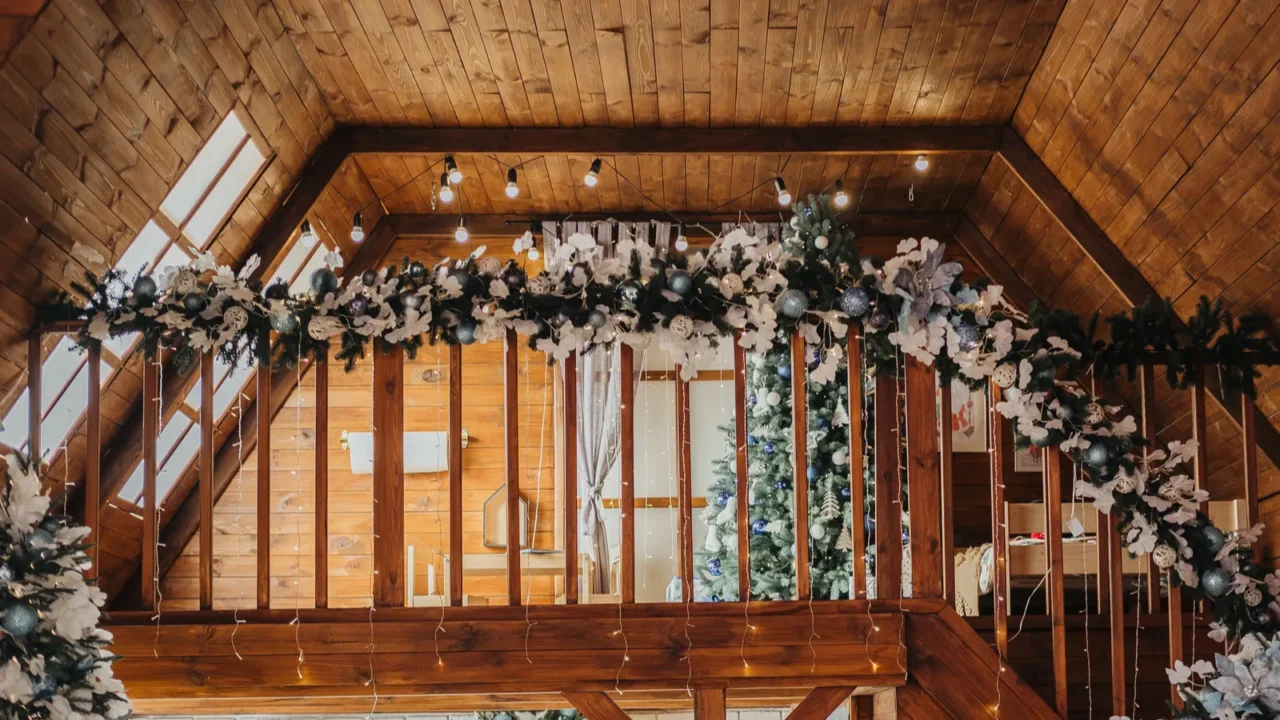 The cozy interior of a wooden cabin showcases festive decorations, including garland and Christmas trees, creating a warm atmosphere perfect for the holiday season.