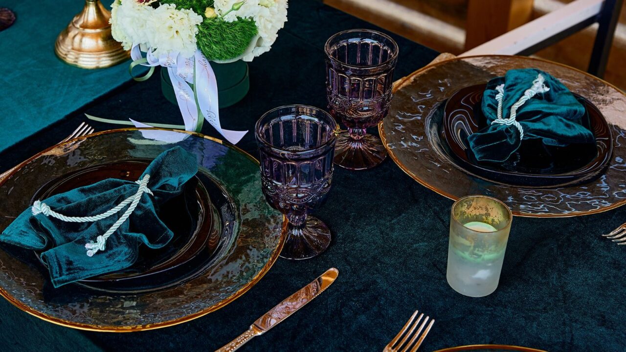 Colored purple glasses, golden candlestick and green velvet napkins and table cloth. Beautiful decorated tableware.