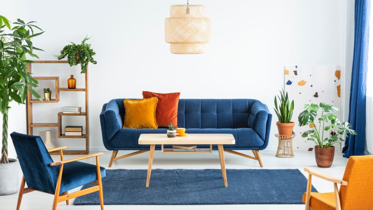 A living room interior with blue sofa with cushions, armchairs, statement ceiling light, coffee table, and a blue rug.