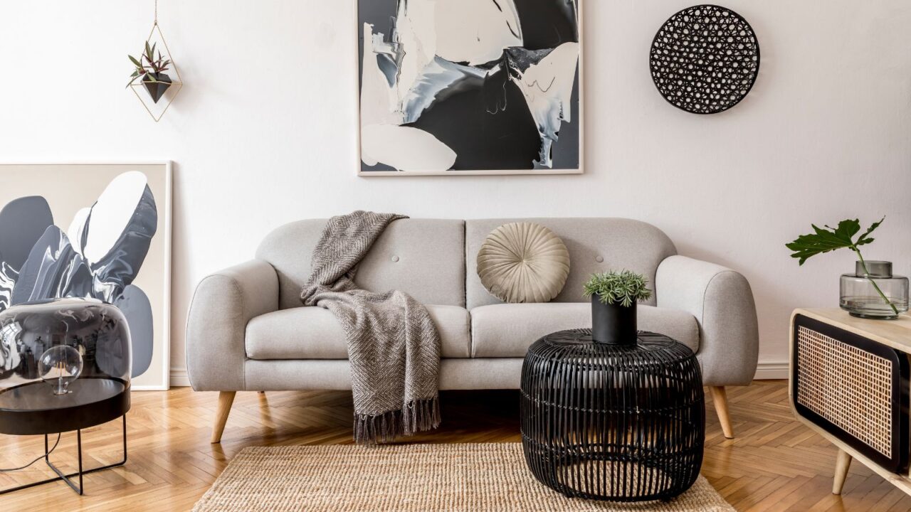 A living room interior with a table, cozy sofa with a throw blanket, plant, and art works on the wall.