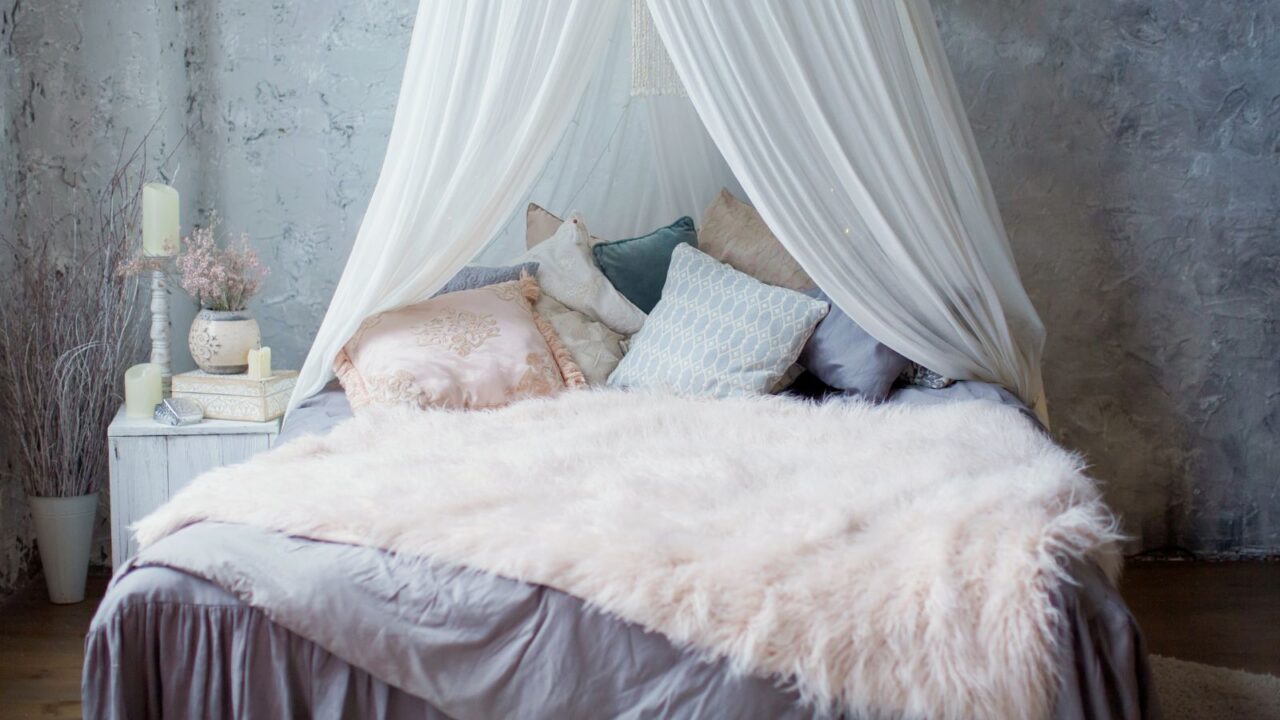 A cozy bed with canopy, cushions, pillows, and faux fur throw blanket.