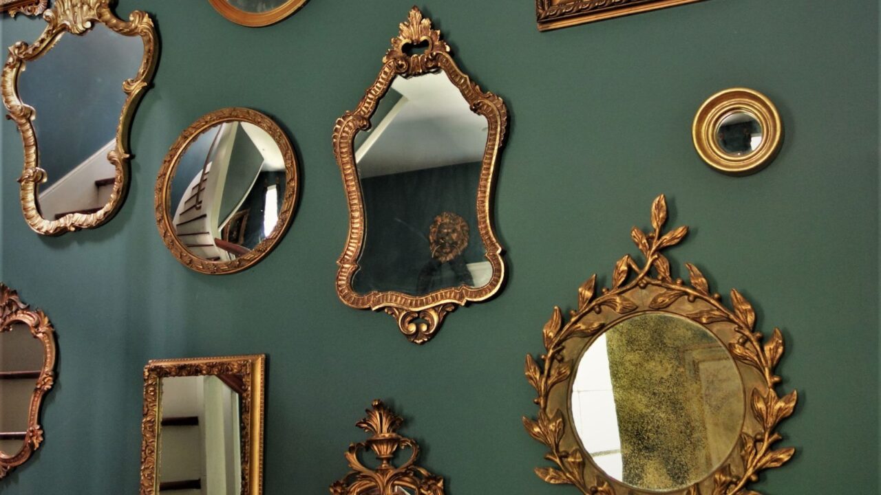 Vintage mirrors of different shapes and sizes with metallic frames hanging on a green wall.