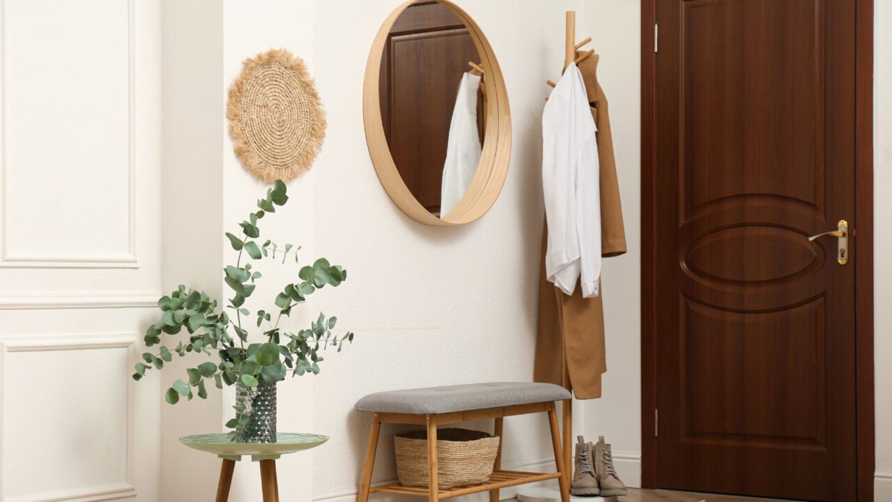 A stylish entryway with a bench, mirror, plant, and a coat stand.