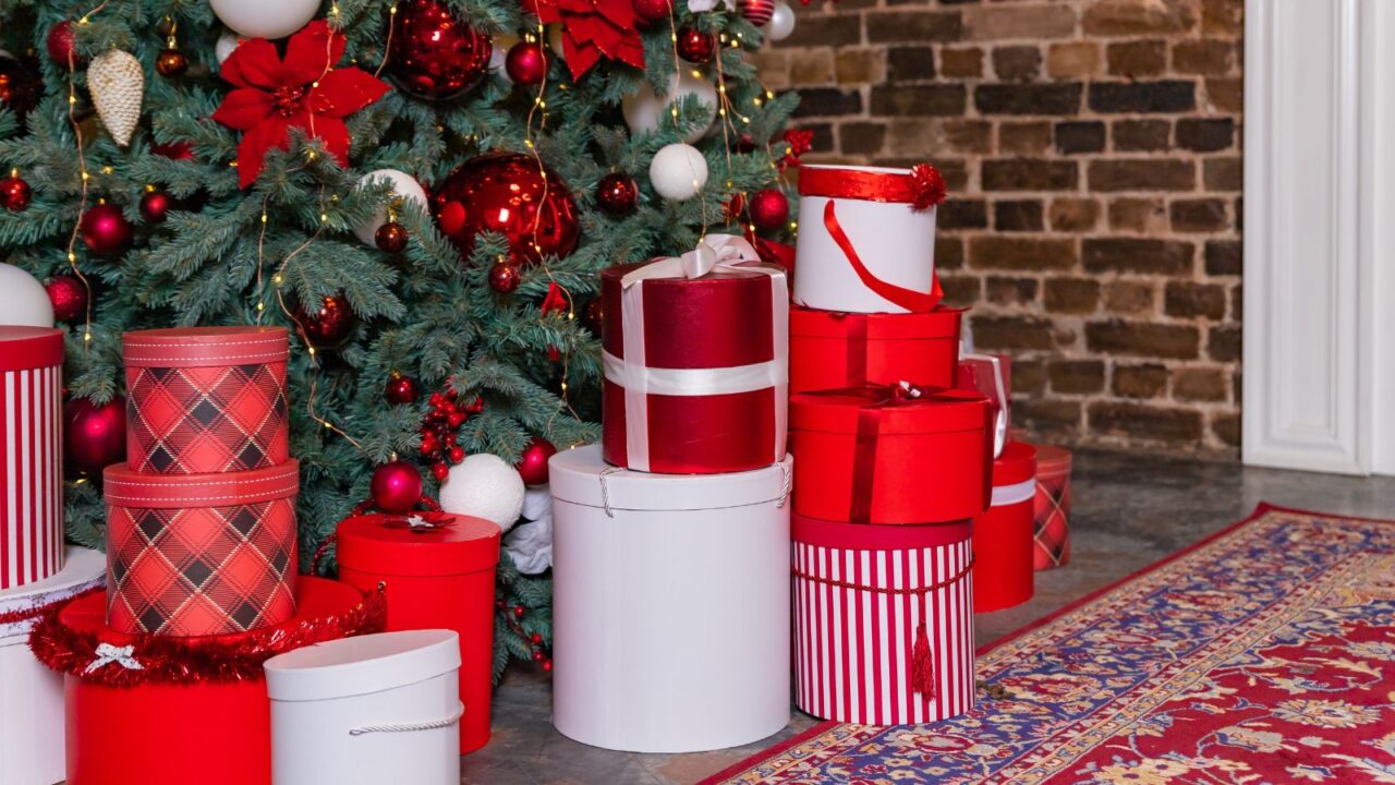 A christmas tree, gifts and a rug in front of a brick wall.