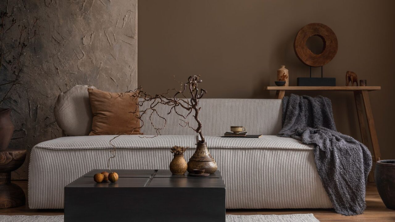 A neutral living room interior with a cozy sofa, throw blanket, coffee table, pillow, decor accents, and a wooden console table.