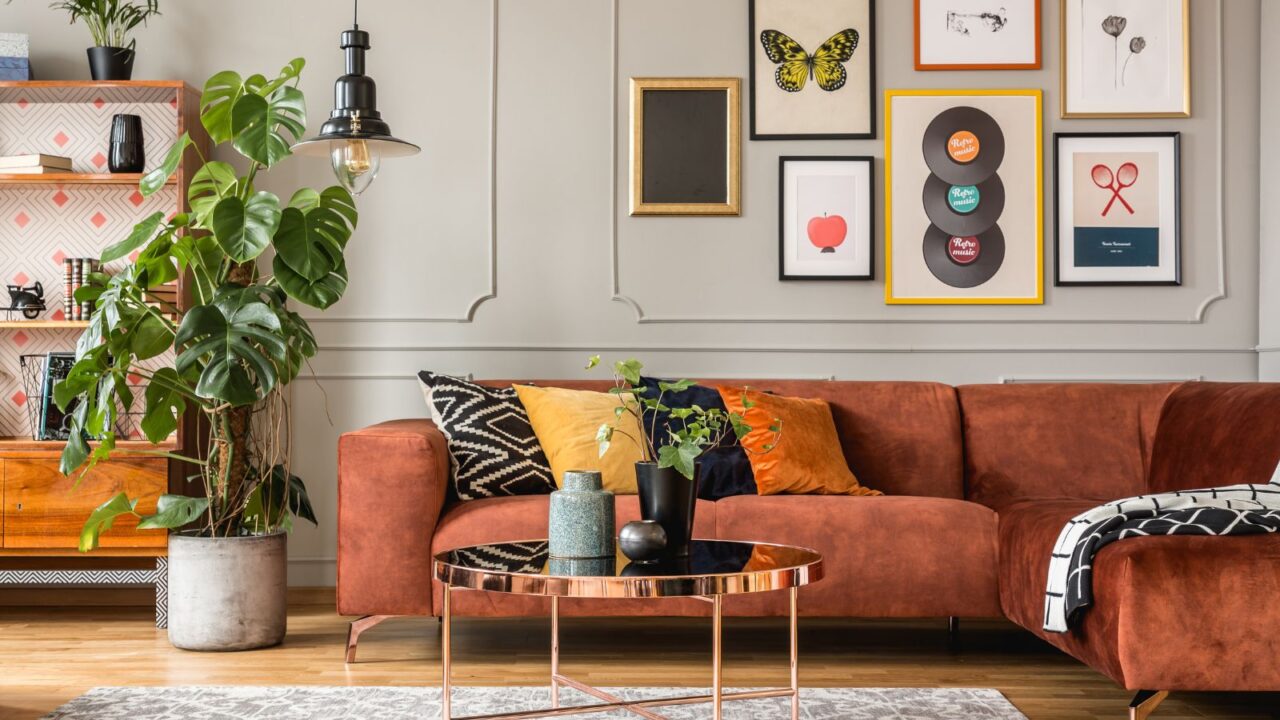 A stylish living room interior with a red couch, coffee table, plants, lamp, and art frames.