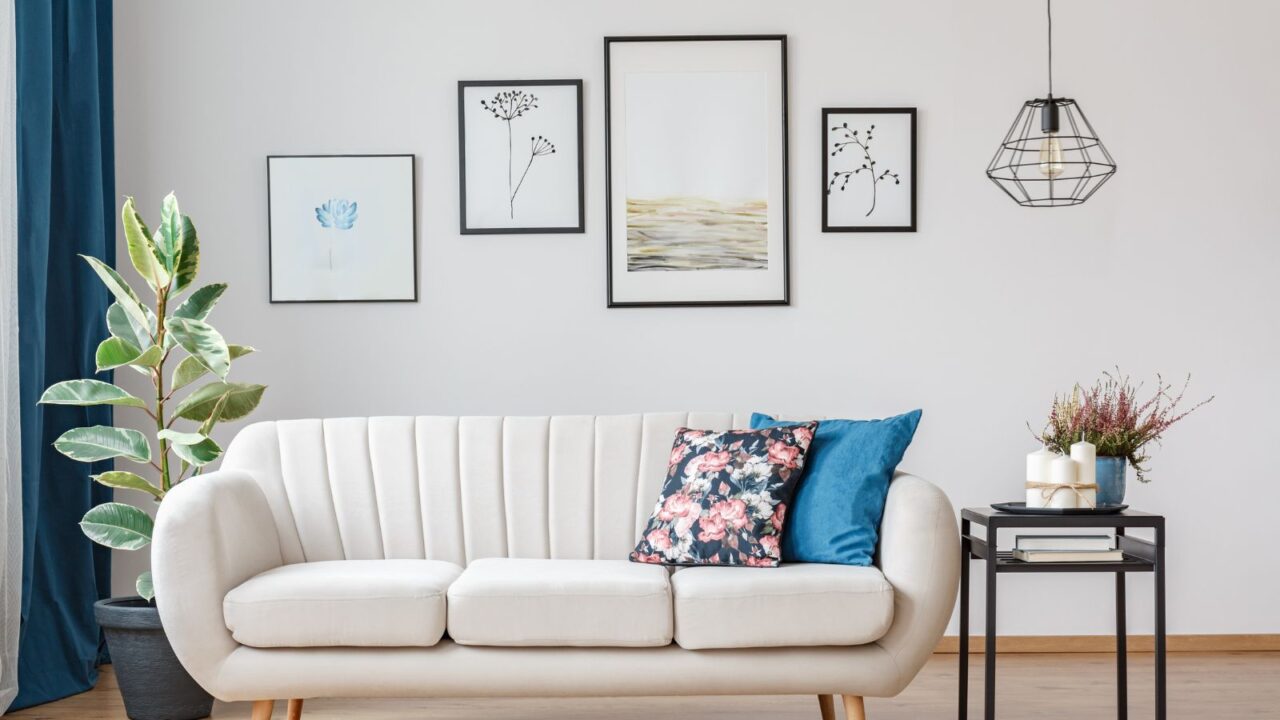 Gallery of posters on white wall in living room interior with beige sofa, ficus and black table.