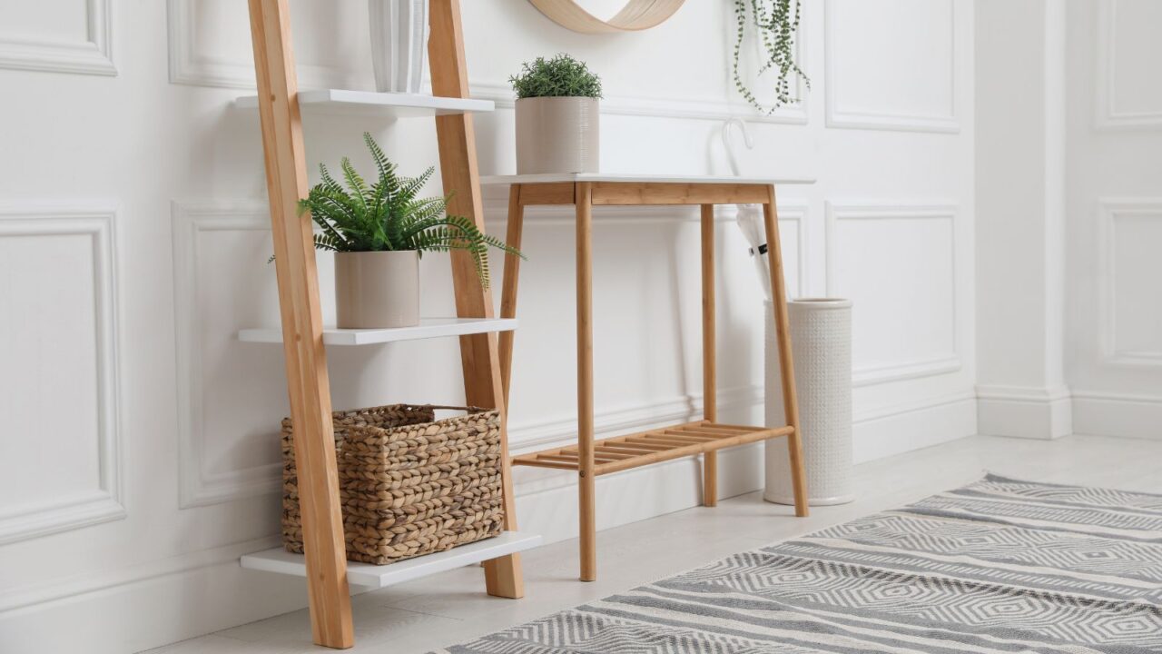 Console table with decorative ladder, storage basket, and mirror on white wall in hallway. Interior design.