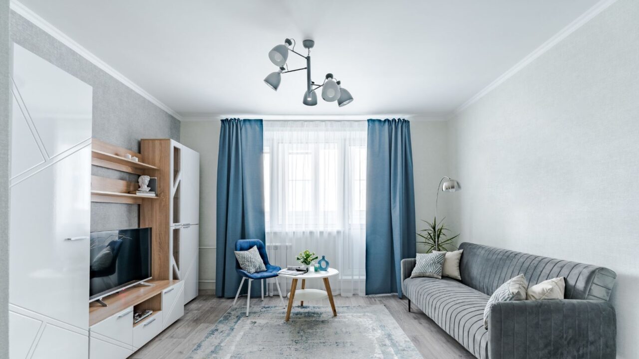 The interior of a small living room in European style apartment. The living room has a wardrobe for storing things, a TV, a coffee table, sofa and an armchair.