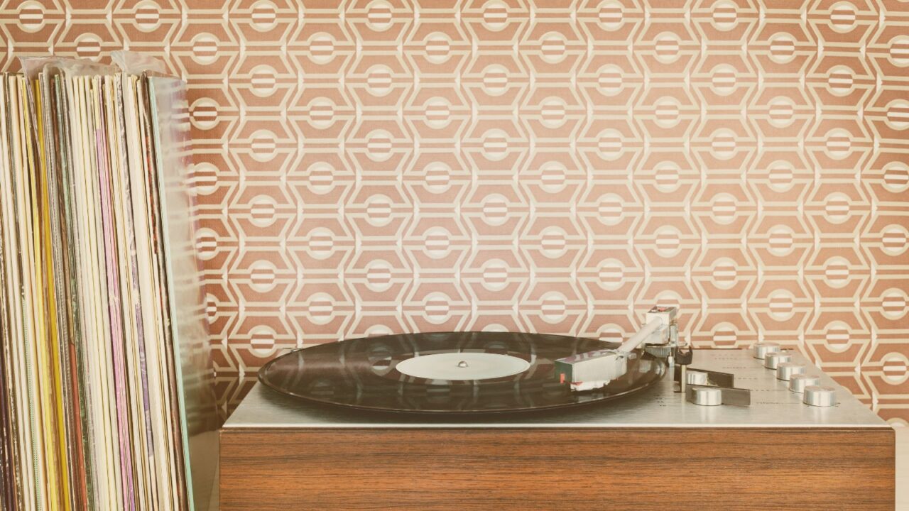 Retro styled image of a vintage record player with record albums in front of 70s wallpaper.