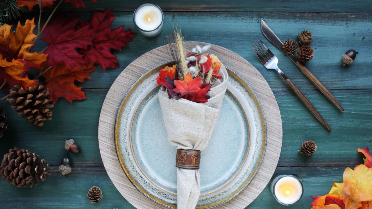 A holiday place setting with plate, napkin, and silverware on a a blue Thanksgiving decorated table shot from flat lay or top view position.