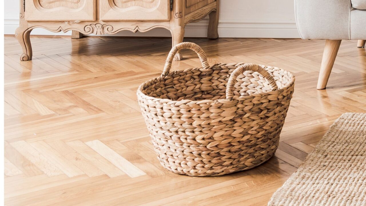 A woven basket on a wooden floor next to an antique cabinet.