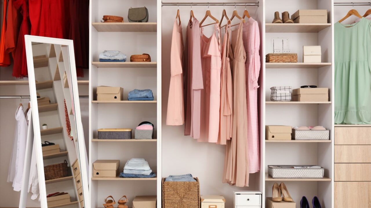 A closet with dresses, mirror, bags and shoes.