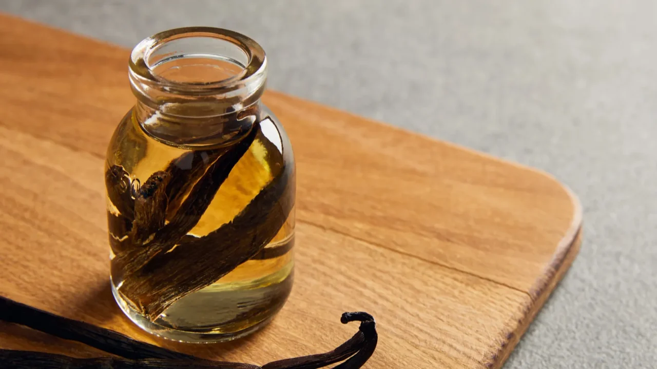 Vanilla pods and essential oil on wooden cutting board on dark surface.