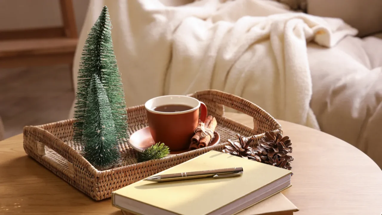 Wooden coffee table with books, mini Christmas trees and cup of tea in interior of light living room