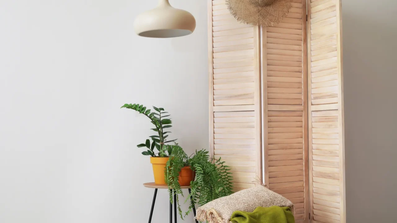 Wooden folding screen with plants on table and wicker basket near light wall in living room