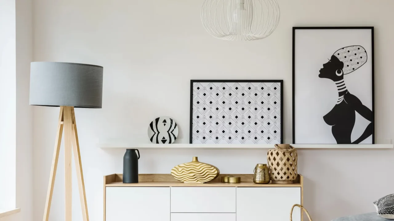 Wooden table and grey pouf in bright flat interior with posters and lamp next to cabinet. Real photo