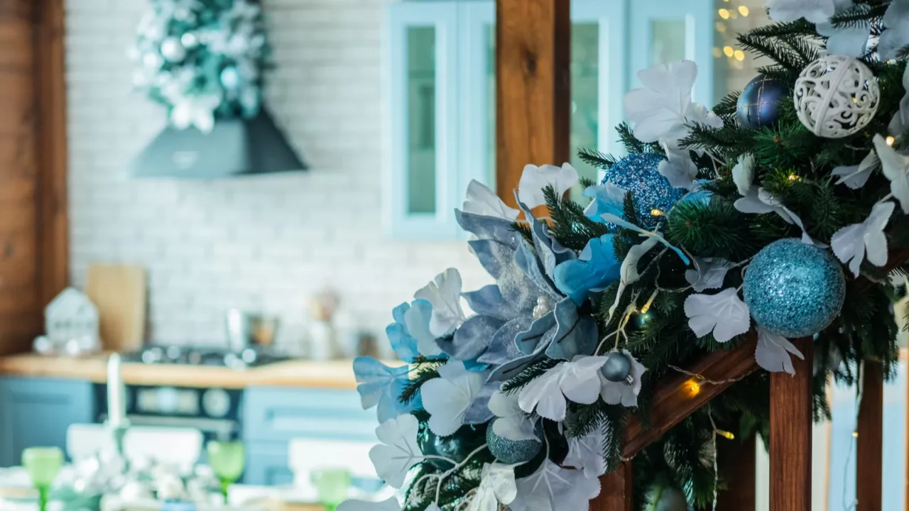 A cozy dining area and staircase adorned with blue and white garland. Blue kitchen in the background.