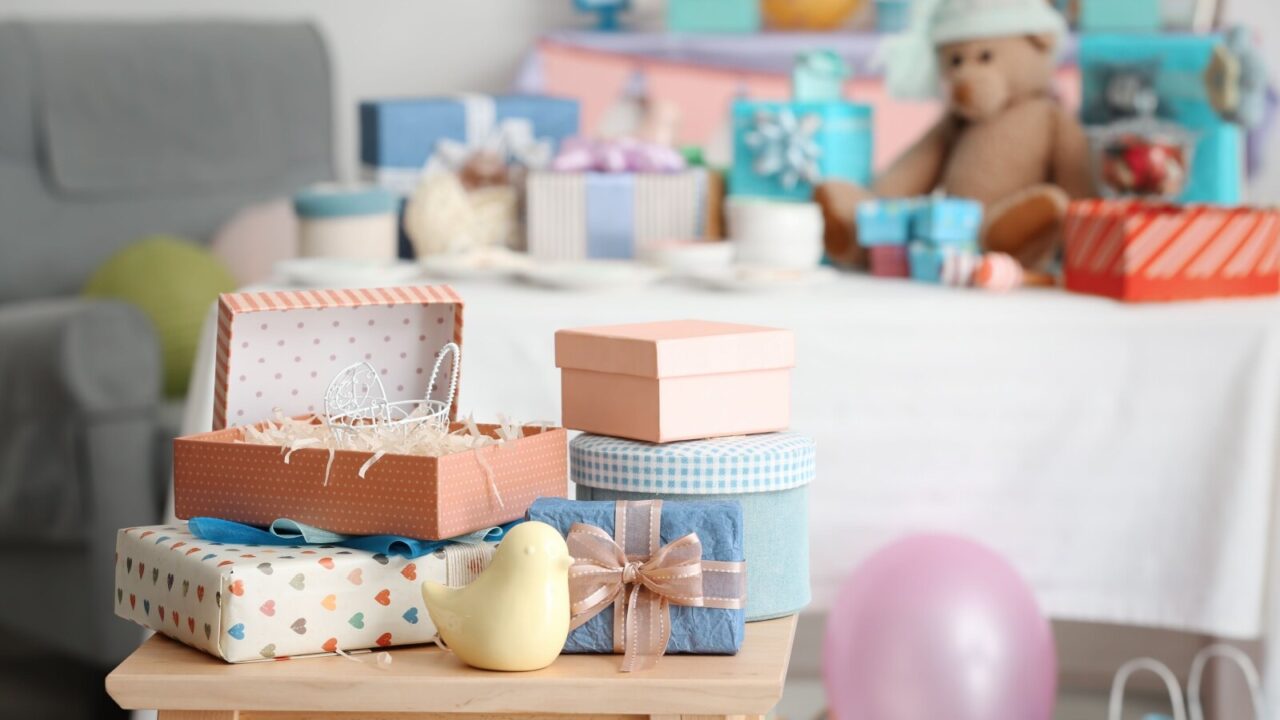 Baby shower gifts placed on a wooden stool in the living room with even more gifts placed on a table in the background