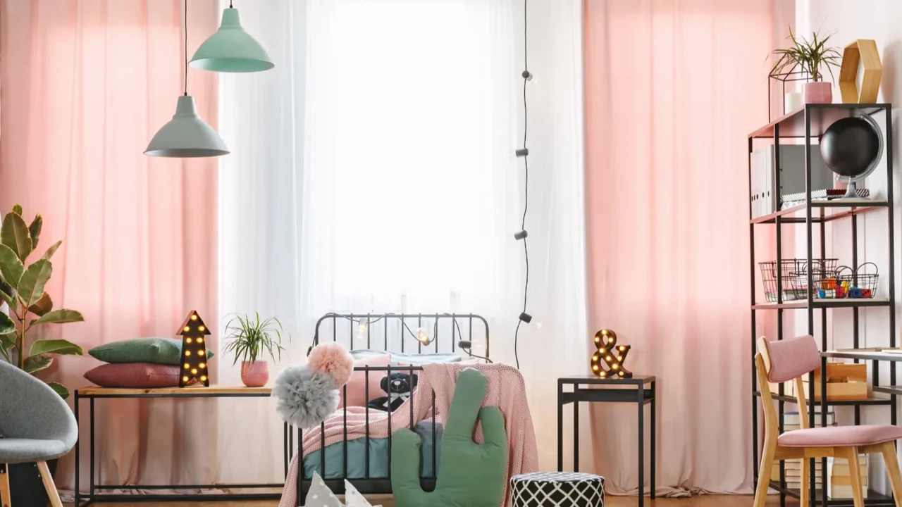 A colorful room with a bed, green chair, plants, and hanging lights near large windows.