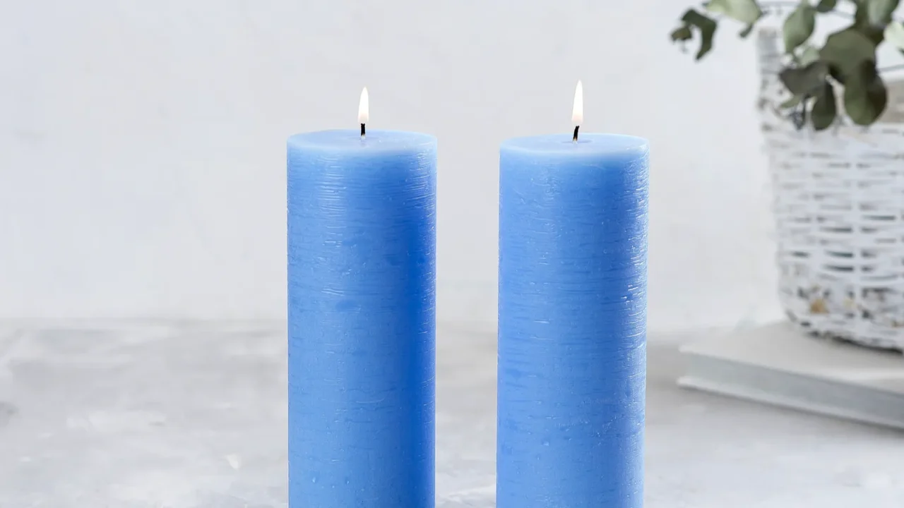 Blue candles placed in the foreground and beautiful green flowers in a basket light gray in background.