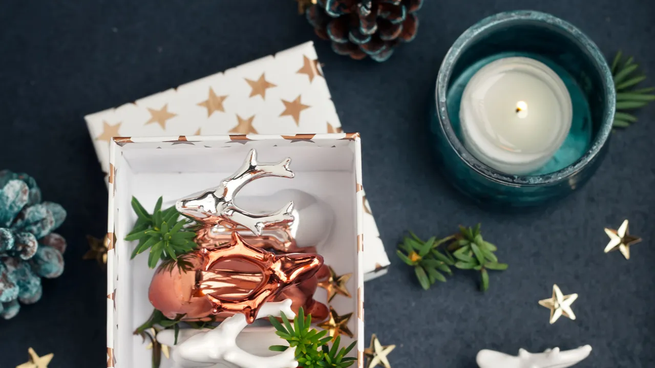 Christmas decor with teal candle holder and copper ceramic reindeer, gift boxes, pinecones, and gold stars.