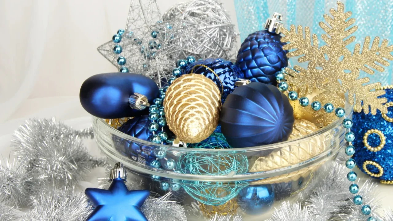 Blue, silver, and gold baubles and Christmas decorations in glass bowl.