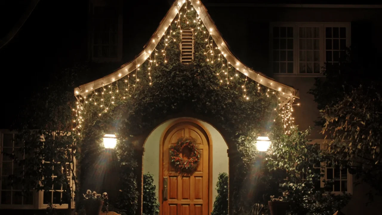 A cozy home entrance adorned with warm holiday lights and a decorative wreath, set against a dark night.