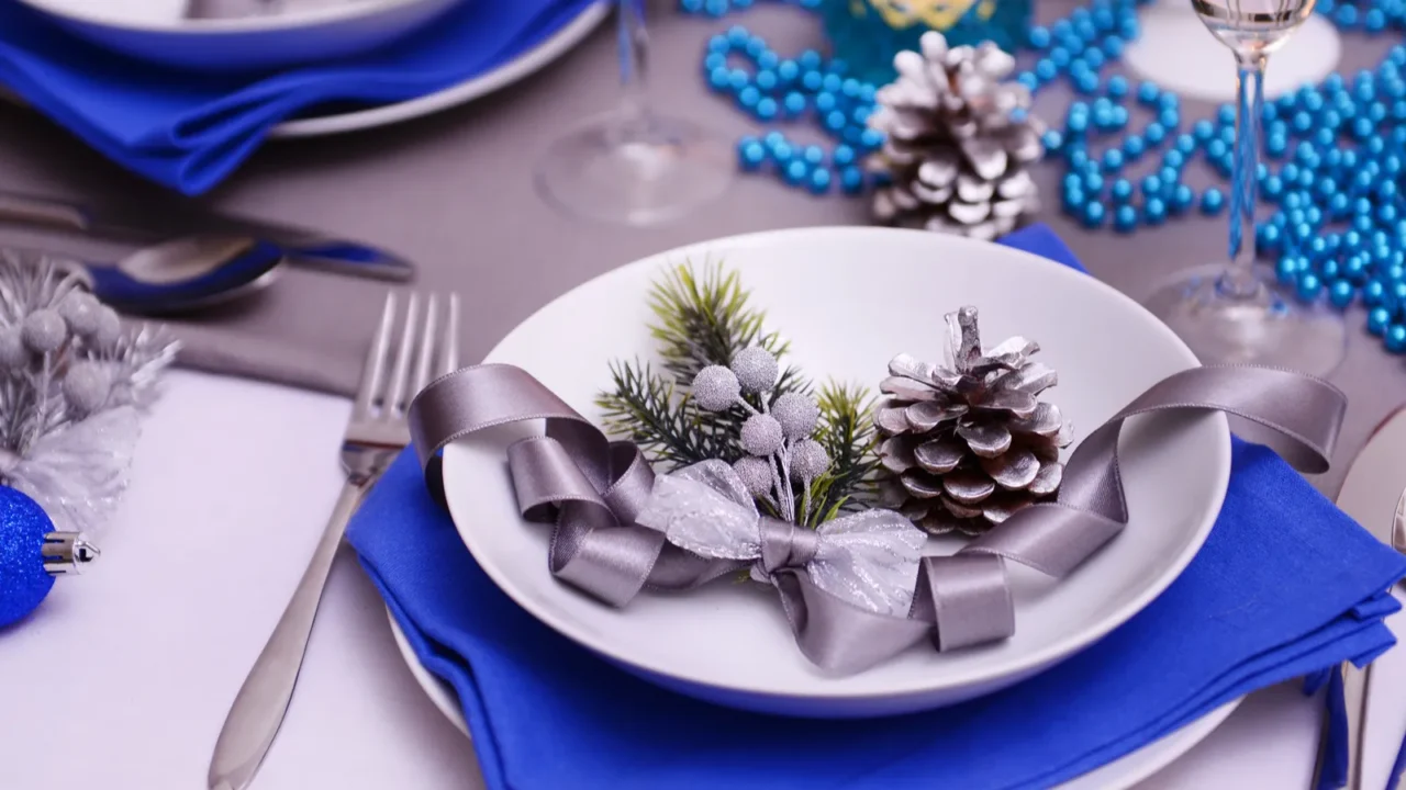 Blue table napkins and decor on dining table with pinecones and silver ribbon on the plate.