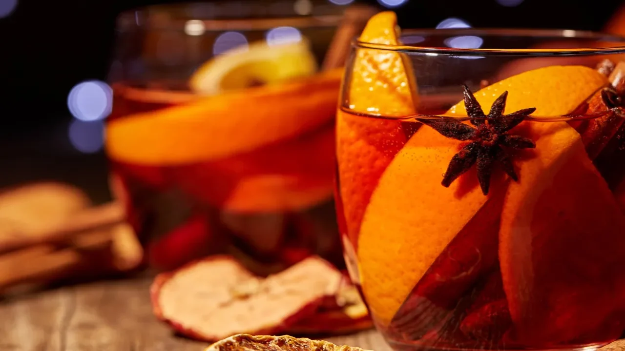 Close up view of delicious hot mulled wine drinks and spices on wooden tabletop with defocused bokeh lights on background.