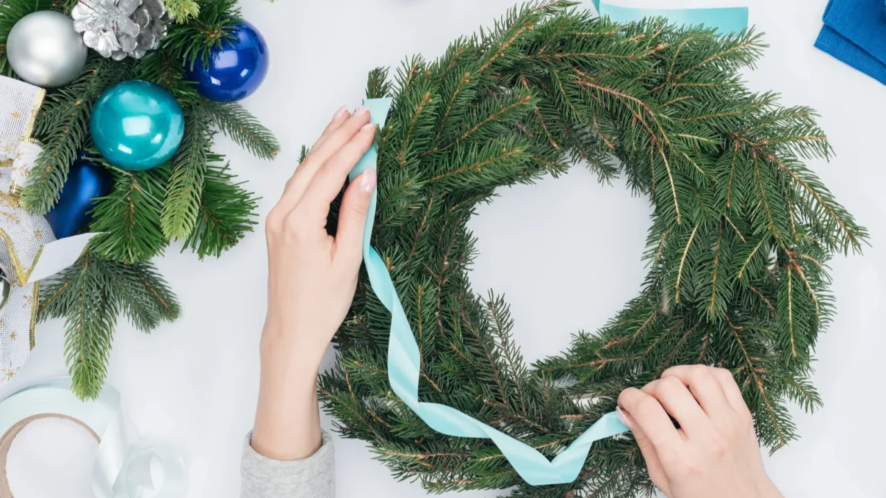 Woman decorating handmade Christmas wreath with blue ribbon. Blue baubles in the background.