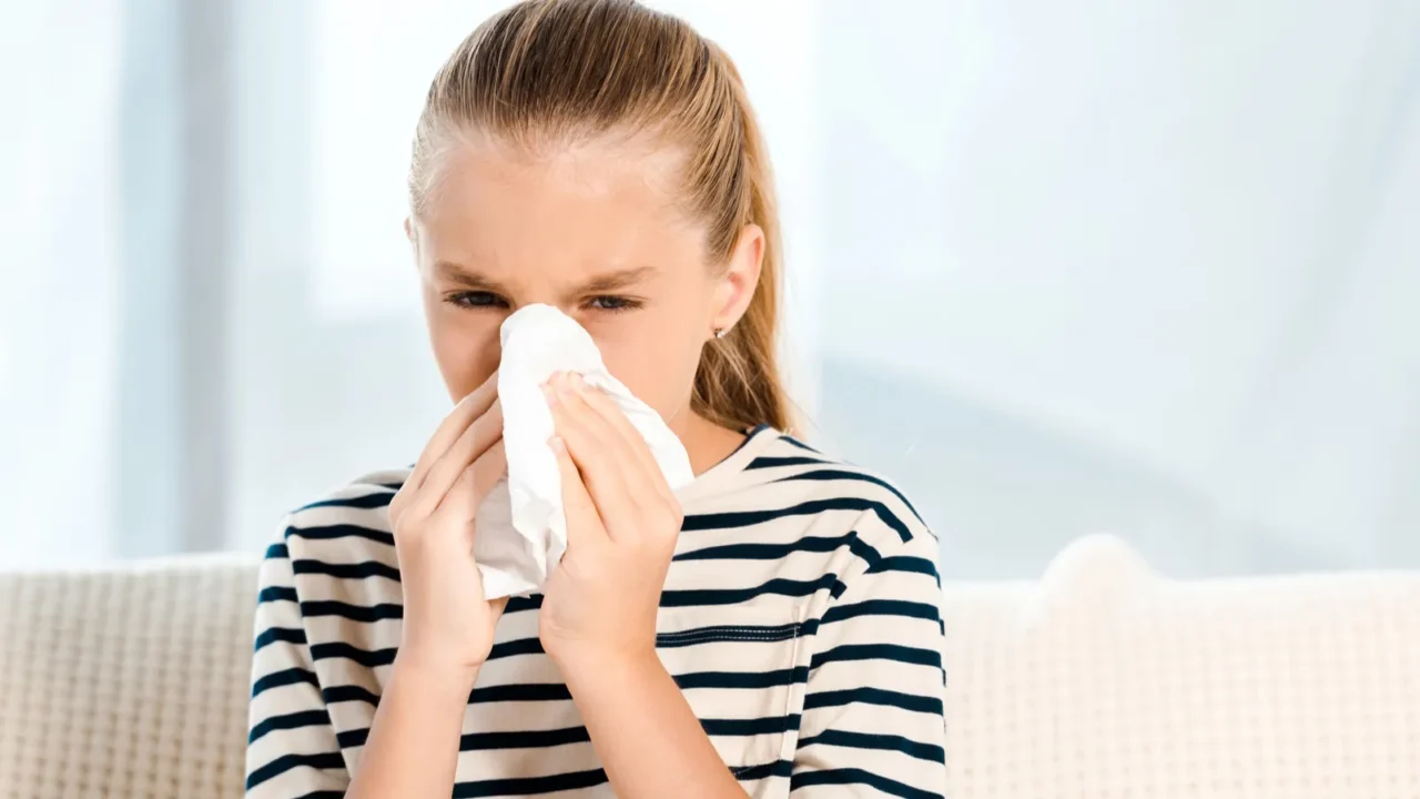 diseased kid sneezing in tissue and looking at camera